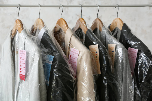 Rack mit sauberen Jacken in Plastiktüten auf Grunge-Hintergrund, Nahaufnahme - Foto, Bild