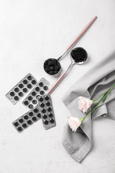 Activated carbon pills, napkin and flowers on light background - Photo, Image