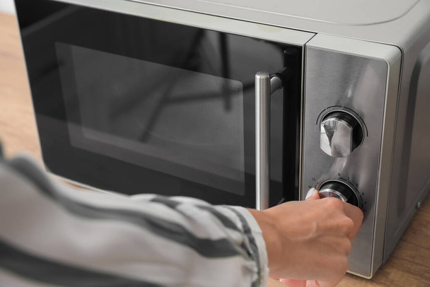 Woman using modern microwave oven on counter in kitchen - Φωτογραφία, εικόνα