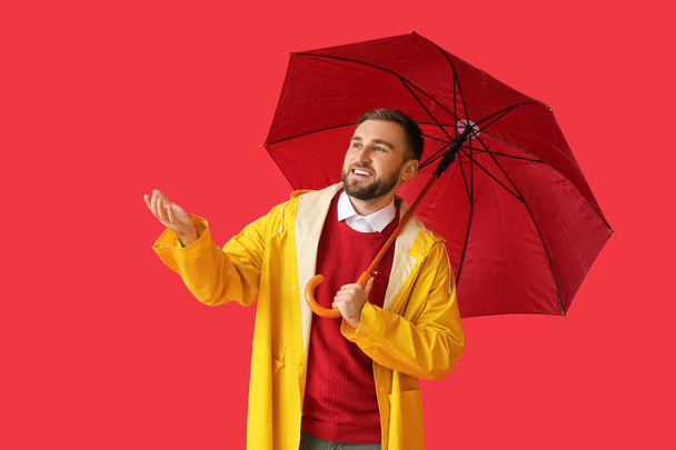Mladý muž ve stylovém plášti a s deštníkem na barevném pozadí - Fotografie, Obrázek