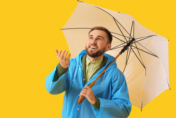 Νεαρός άνδρας με κομψό αδιάβροχο και ομπρέλα στο φόντο χρώμα - Φωτογραφία, εικόνα