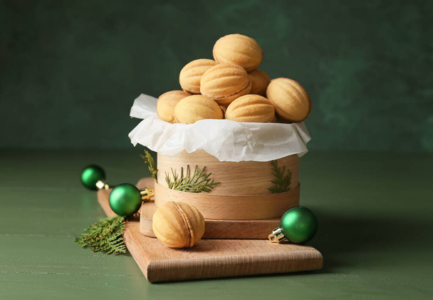 Caja llena de sabrosas galletas en forma de nuez con leche condensada hervida, ramas de thuja y bolas de Navidad en la mesa de madera de color - Foto, imagen
