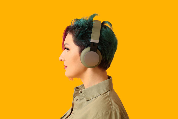 Schöne Frau mit ungewöhnlichen Haaren hört Musik auf gelbem Hintergrund - Foto, Bild