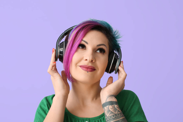 Piękna kobieta z nietypowymi włosami i tatuażem słuchająca muzyki na kolorowym tle - Zdjęcie, obraz