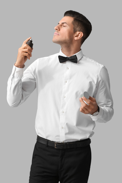 Caballero de moda rociando perfume sobre fondo gris - Foto, imagen