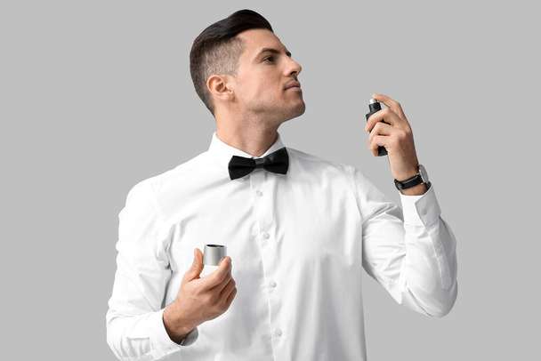 Fashionable young gentleman spraying perfume on grey background - 写真・画像
