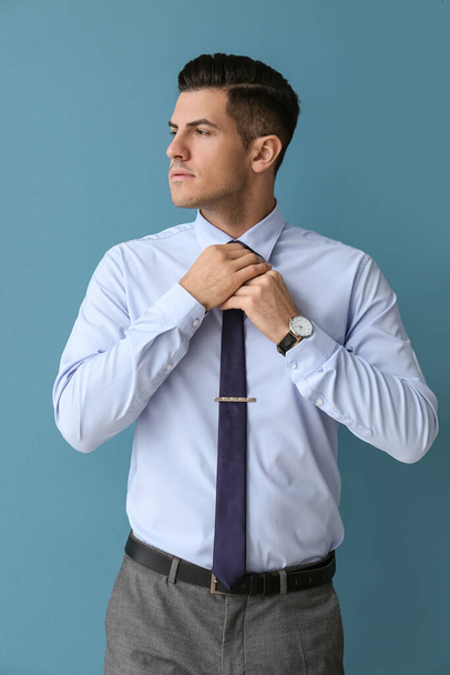 Handsome man in formal clothes looking aside and adjusting tie on color background - Photo, image