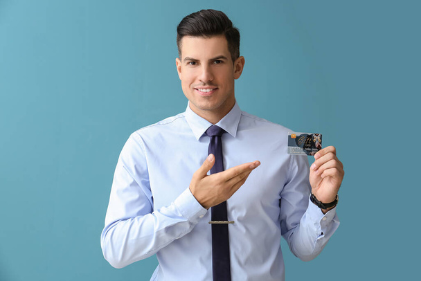 Handsome man in formal clothes pointing at gift card on color background - Fotoğraf, Görsel