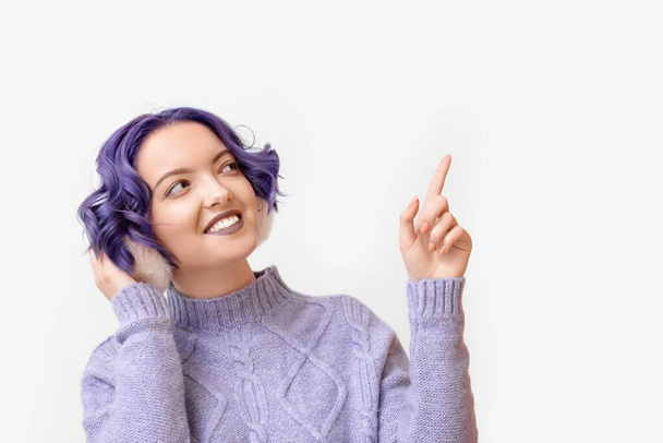 Hermosa mujer joven con el pelo violeta y audífonos esponjosos apuntando a algo en el fondo blanco. Muy Peri - el color del año 2022 - Foto, imagen