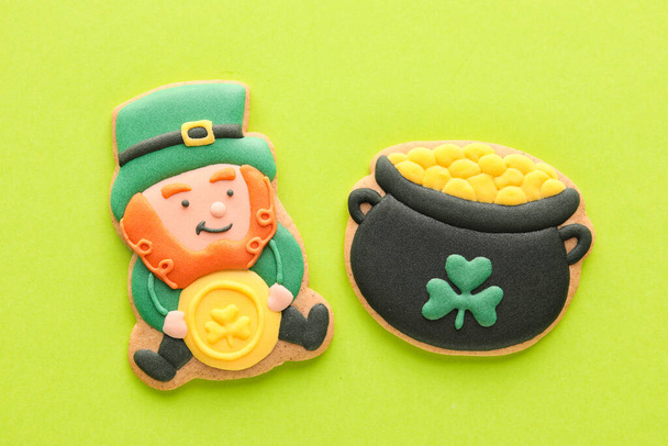 Tasty decorative gingerbread cookies for St. Patrick's Day celebration on green background - 写真・画像