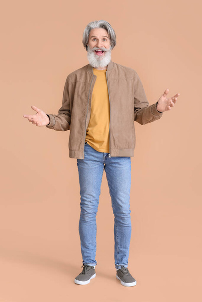 Surprised senior man in stylish jacket on beige background - Fotoğraf, Görsel