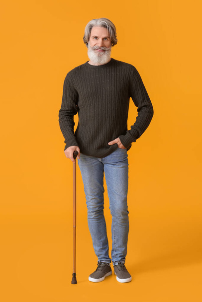 Älterer Mann im Pullover mit Gehstock auf gelbem Hintergrund - Foto, Bild