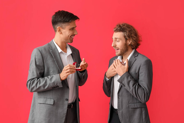 Young gay proposing to his boyfriend on red background - 写真・画像