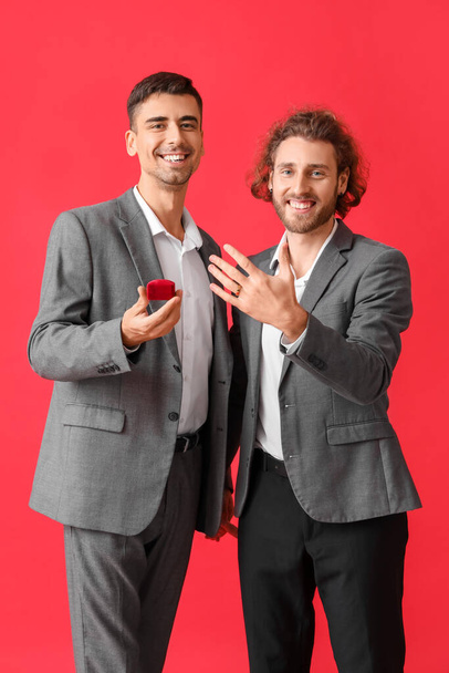 Happy engaged gay couple on red background - Foto, Imagen
