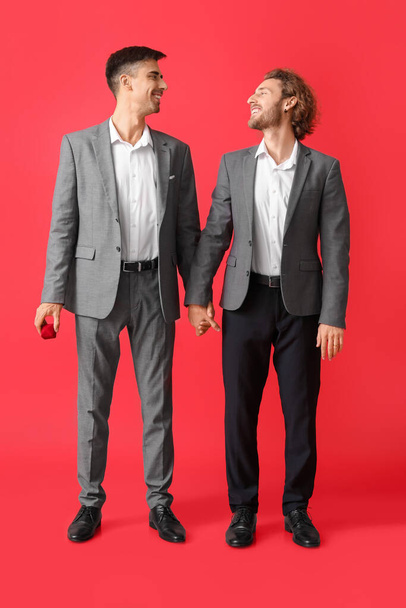 Happy engaged gay couple on red background - Photo, Image