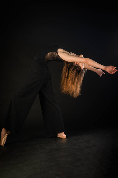 Beautiful ballerina is posing while bending her back on black background - Foto, imagen