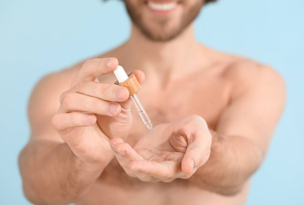 Jongeman met serum voor huidverzorging op kleur achtergrond, close-up - Foto, afbeelding