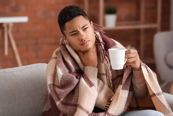 Ill African-American guy with sore throat drinking hot tea at home - Zdjęcie, obraz