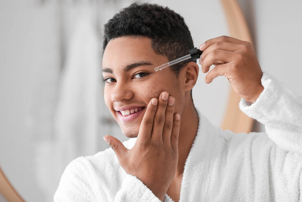 Fiatal afroamerikai fickó, aki szérumot használ a fürdőszobában a bőrápoláshoz. - Fotó, kép