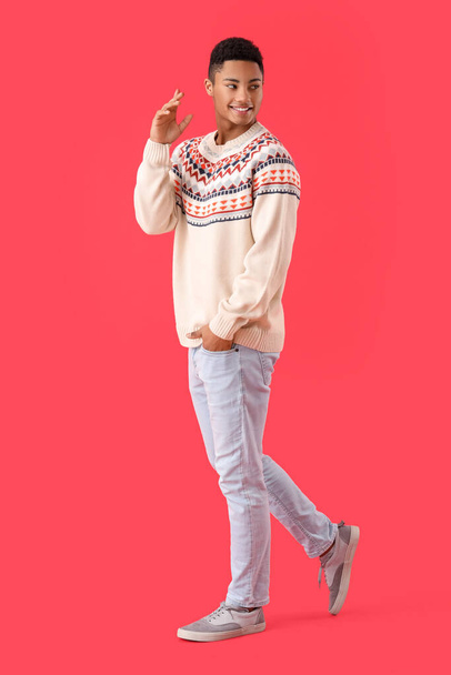 Handsome African-American guy in knitted sweater on red background - Фото, изображение
