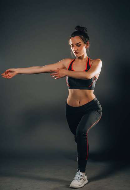 Fitness-Frau beim Stretching-Training. Aufnahme einer jungen Frau auf dunklem Hintergrund in voller Länge. Dehnung und Motivation - Foto, Bild