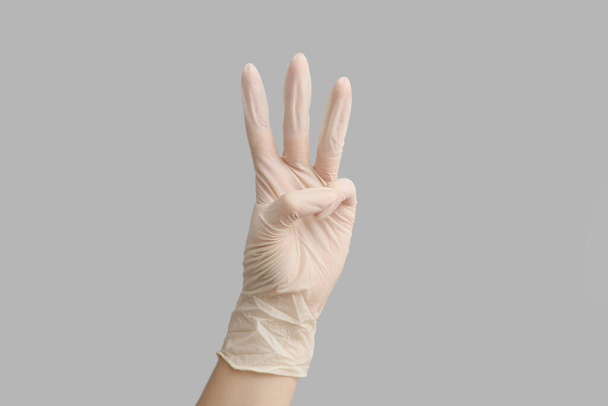 Γυναίκα στο ιατρικό γάντι δείχνει τρία δάχτυλα στο φως φόντο - Φωτογραφία, εικόνα