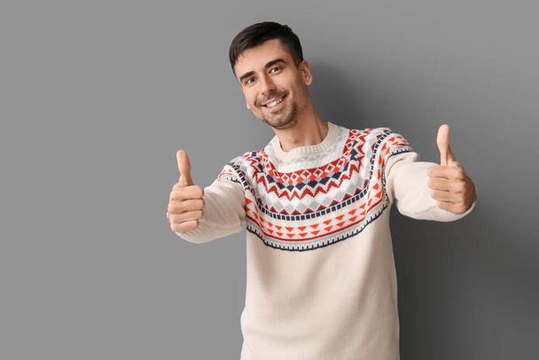 Hezký mladý muž v pleteném svetru ukazující palec nahoru na šedém pozadí - Fotografie, Obrázek