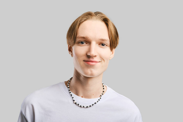 Closeup portrait of smiling young man in white t-shirt over grey studio background - Photo, Image