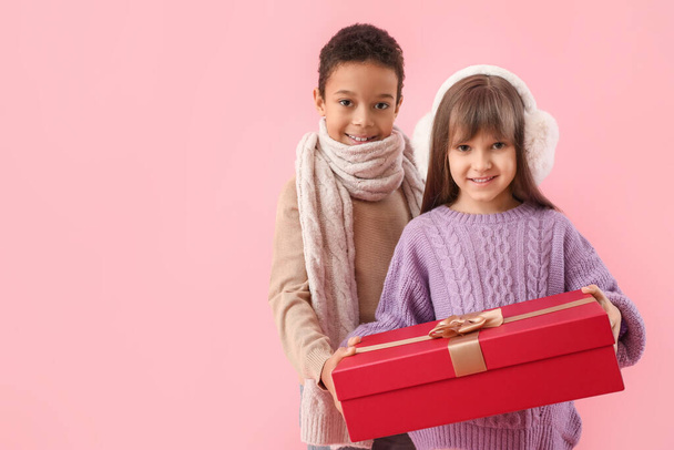 Cute little children in winter sweaters and with gift on color background - Photo, Image