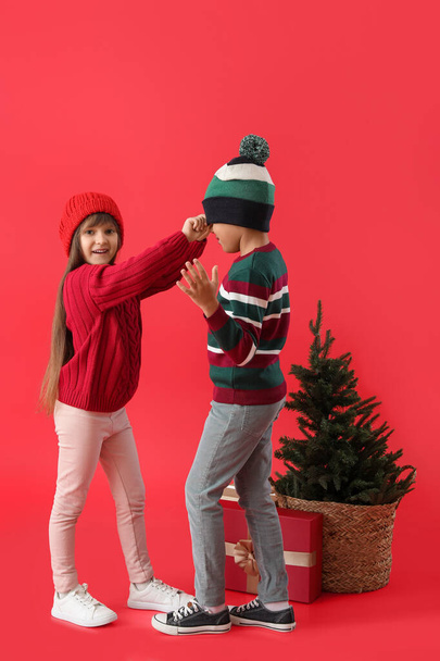 Happy little children in winter clothes, with Christmas tree and gift on color background - Fotoğraf, Görsel