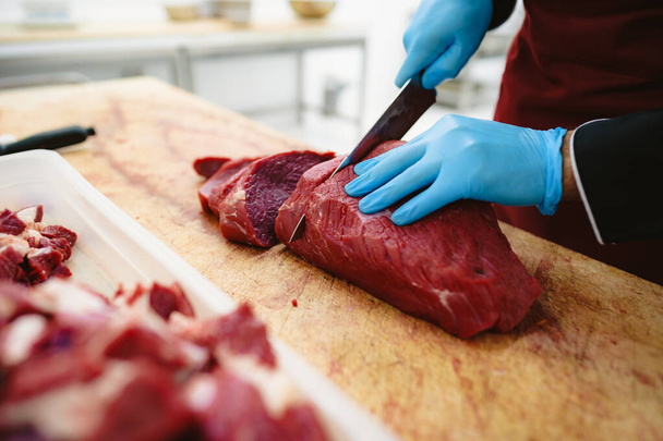 Butcher cutting slices of raw meat on wooden board - Φωτογραφία, εικόνα