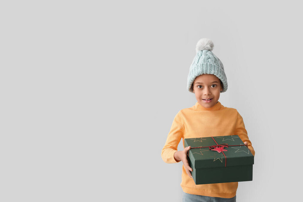 Cute little African-American boy in winter clothes and with Christmas gift on grey background - Photo, image
