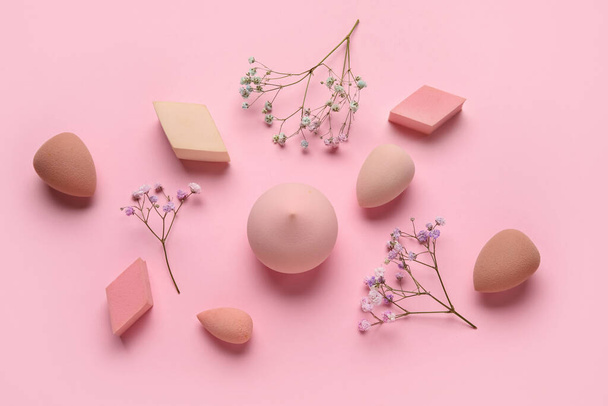 Diferentes esponjas de maquillaje y flores sobre fondo rosa - Foto, Imagen