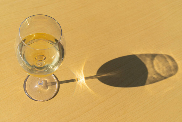 Verre de vin blanc sur fond jaune avec effet d'ombre solaire et espace de copie vide - Photo, image