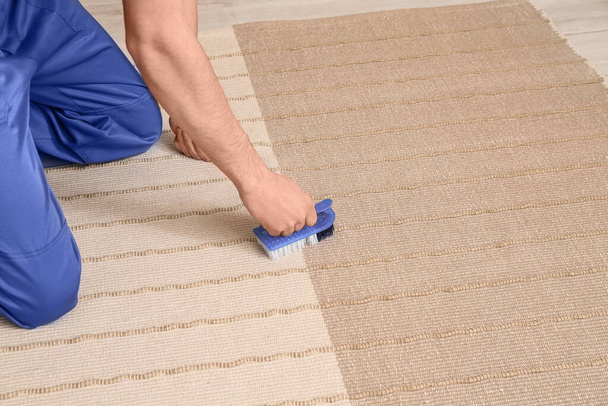 Férfi dolgozó takarítás stílusos szőnyeg kefével a szobában, közelkép - Fotó, kép