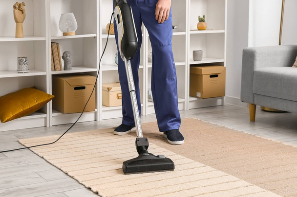 Male worker cleaning stylish carpet in room - Foto, afbeelding