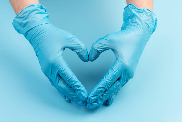 Persona in guanti di lattice che mostra il gesto del cuore contro lo sfondo azzurro, primo piano sulle mani - Foto, immagini