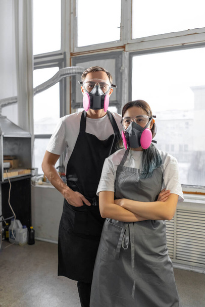 Couple man and woman in pink respirators in a workshop. Respiratory protection. Vertical image. - Foto, Imagem
