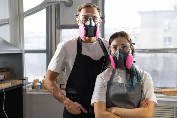 Portrait of man and woman in pink respirators against background of factory window. Workers at factory. - Фото, зображення