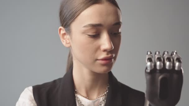 Langzaam close-up portret van lachende jonge blanke vrouw met zwarte bionische arm kijkend naar camera op grijze achtergrond - Video