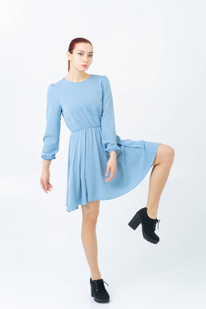 An Asian woman poses in a studio in blue summer dress and black shoes. Looks at camera. White background. - Foto, Imagem