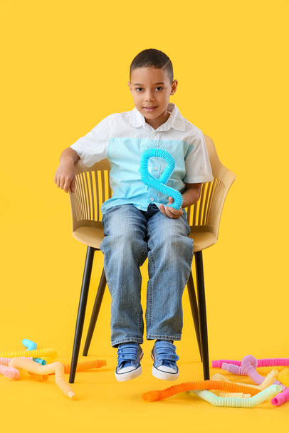 Kis afro-amerikai fiú Pop Tubes ül székben sárga háttér - Fotó, kép