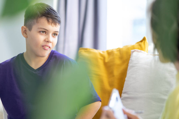 Cheerful smiling teenager in purple T-shirt talks to child psychologist. Blurred foreground. - Фото, зображення