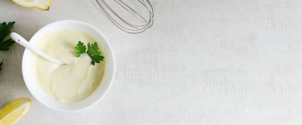 Homemade mayonnaise in a white bowl with parsley leaf and lemons in the background. The concept of proper nutrition. Top view. copy space. Horizontal orientation. Banner. - Photo, Image