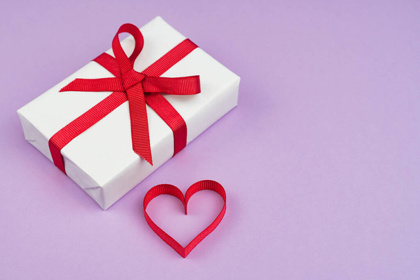 Valentines Day or birthday concept with copy space. Red ribbon heart and gift box on purple papper - Fotoğraf, Görsel