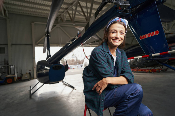 Beautiful smiling brunette airframe engineer sitting in the aviation garage - Photo, Image