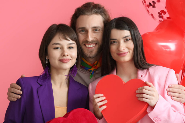 Man and two beautiful women with gifts for Valentine's Day on color background. Polyamory concept - Photo, Image