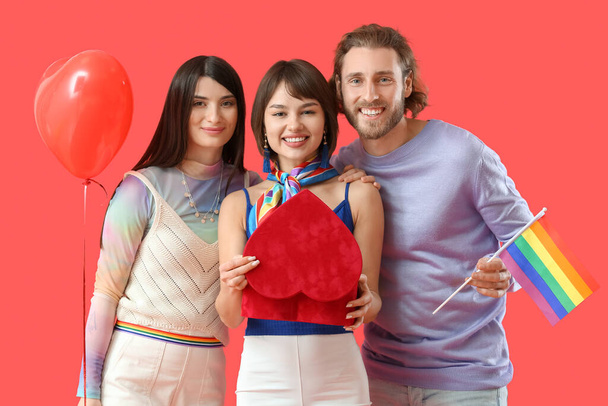 Man and two beautiful women with rainbow flag, gift and balloon on color background. Concept of polyamory and LGBT - Photo, Image