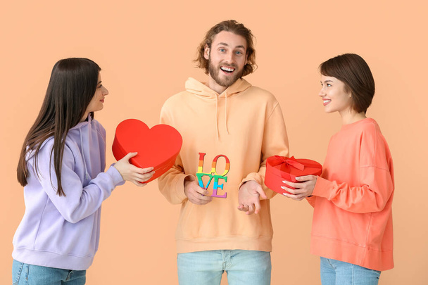 Két gyönyörű nő köszönti a férfit Valentin-napra, színes háttérrel. A poliamória és az LMBT fogalma - Fotó, kép