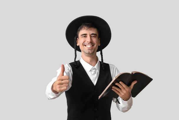 Chassidische joodse man met Thora die duim-omhoog op lichte achtergrond toont - Foto, afbeelding